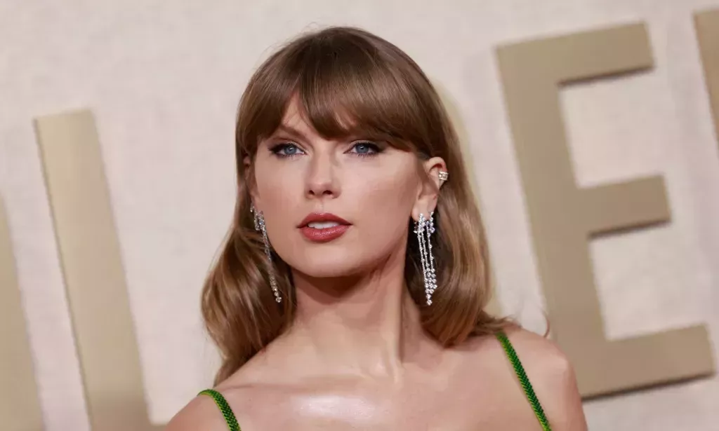 Taylor Swift looks towards the camera while wearing a green dress and long silver dangling earrings