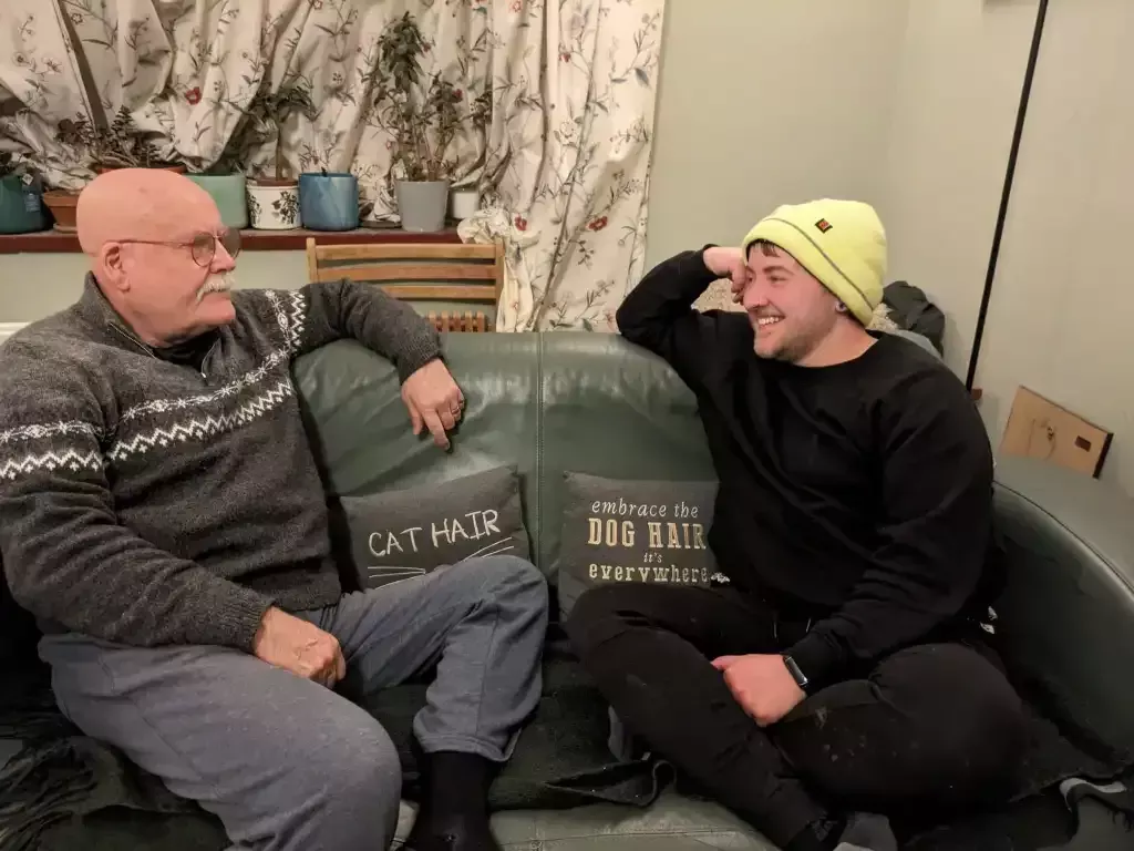 A father and son look at each other while sat on a sofa. 