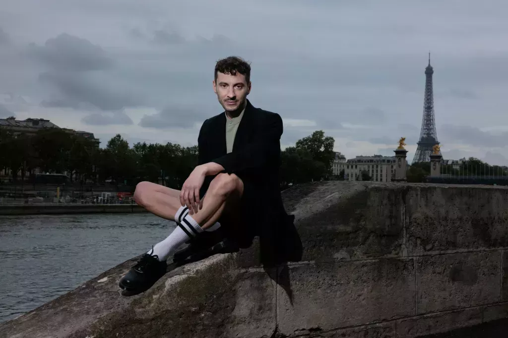 French artistic director for the opening and closing ceremonies of the Paris 2024 Olympic and Paralympic Games Thomas Jolly, poses sitting on a wall near the Seine River with the Eiffel tower in the background.