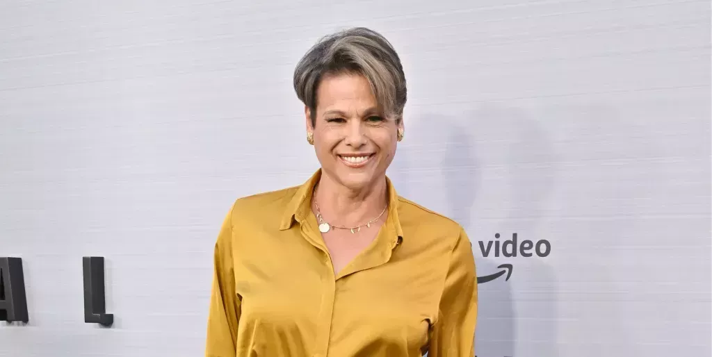 Alexandra Billings smiles while wearing a yellow top on a red carpet