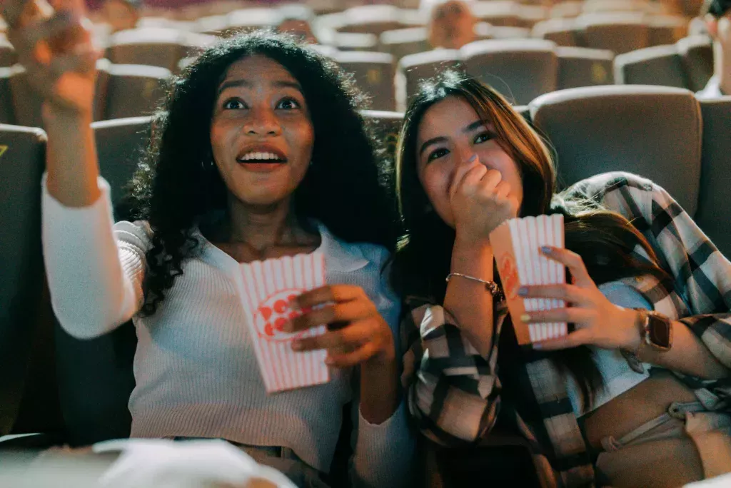 Group of friends of different genders are sitting together chatting happily in a cinema while eating popcorn.