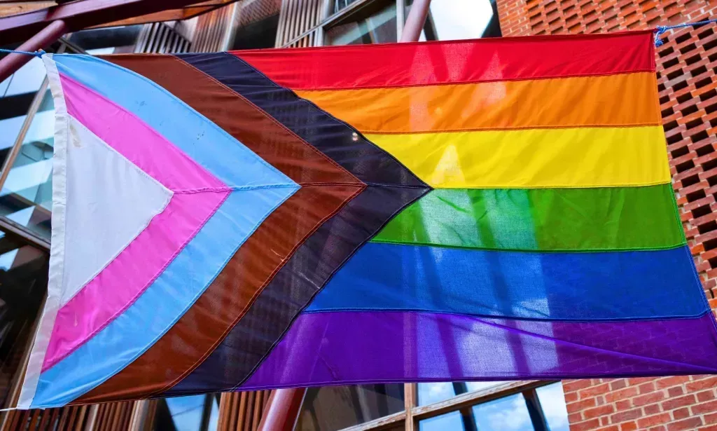 A Progress Pride flag waving in a street.