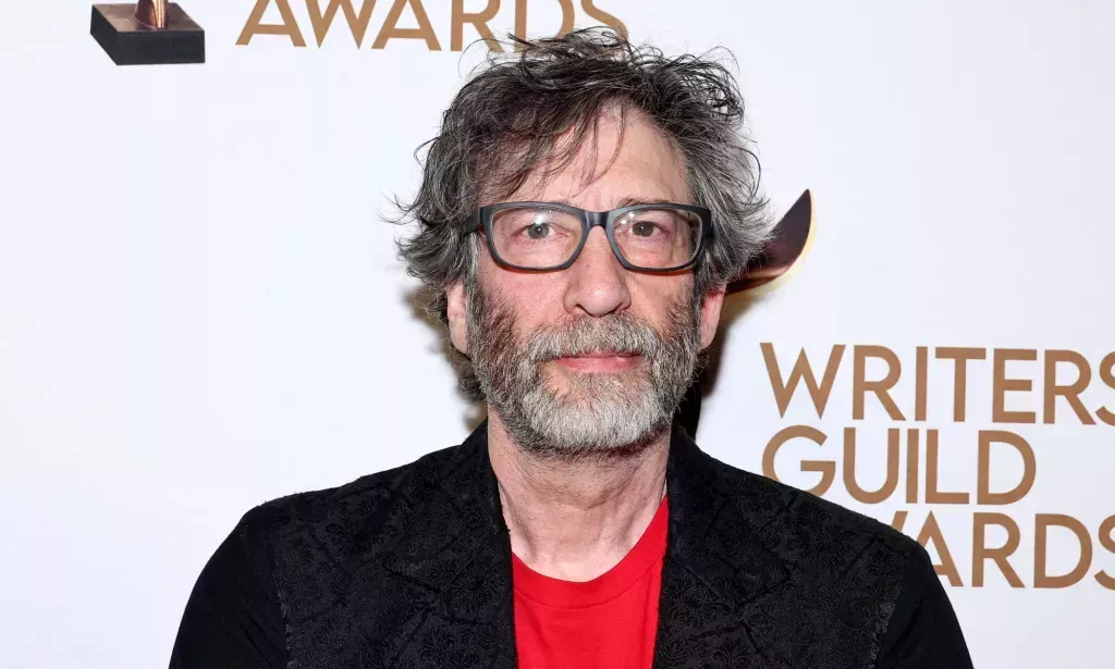 Neil Gaiman en un blazer negro, camiseta roja, gafas.