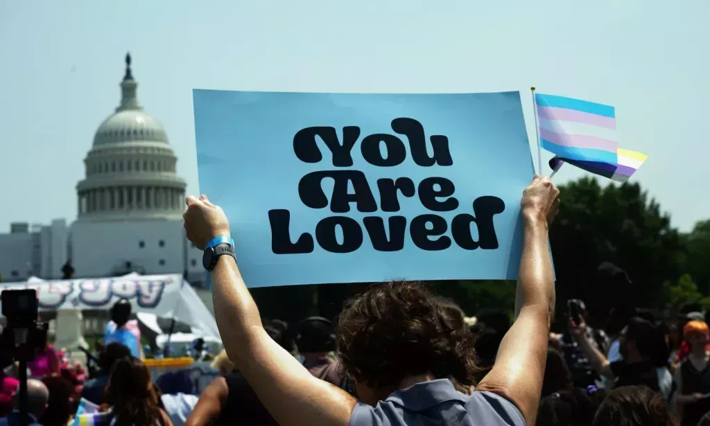 Trans youth hold up a sign reading "you are loved" during a protest.