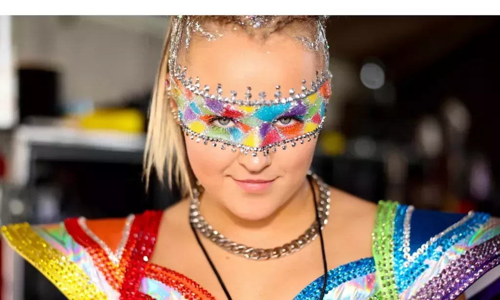 JoJo Siwa vestida con un traje de concierto de arcoíris y un maquillaje de arcoíris en los ojos.