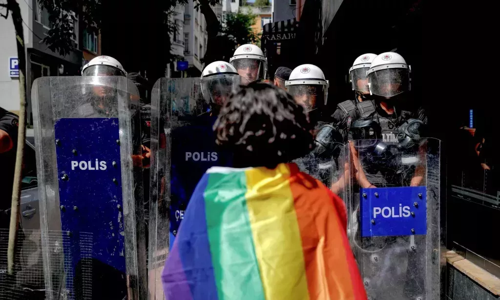 Una persona LGBTQ+ con una bandera del Orgullo sobre los hombros enfrentándose a la policía en Turquía.